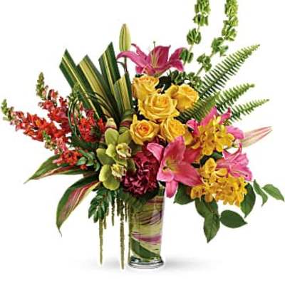 Tall tropical-style arrangement with pink lilies, yellow roses, orchids, and mixed blooms in a clear glass vase