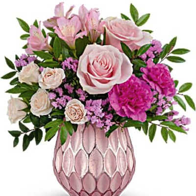 Pink and cream roses, carnations, and mixed blooms arranged in a pink textured glass vase