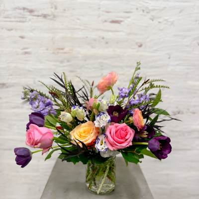 Mixed bouquet of pink, purple, and peach flowers in a glass vase