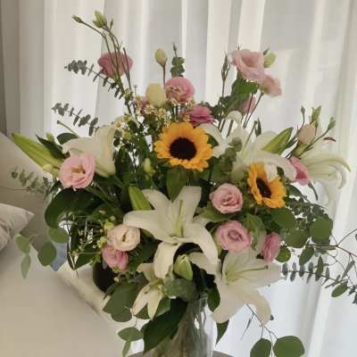 Mixed bouquet with white lilies, pink blooms, and sunflowers in a glass vase