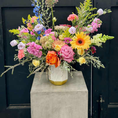 Mixed bouquet in a white vase with pink, yellow, orange, and blue flowers