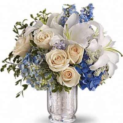 White lilies, cream roses, and blue hydrangeas arranged in a silver glass vase
