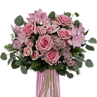 Tall pink vase filled with pink roses, alstroemeria, and filler flowers in a rounded arrangement.