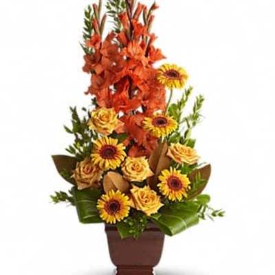 Tall orange and yellow flower arrangement with roses and daisy-like blooms in a brown vase