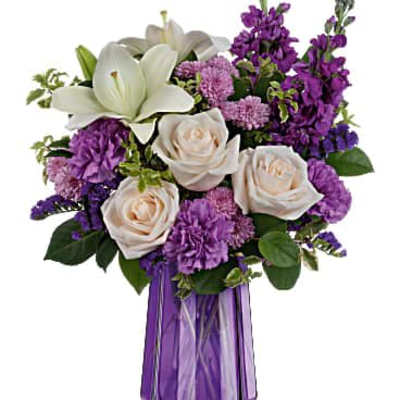 Purple and white mixed flower arrangement with lilies and roses in a tall faceted purple glass vase