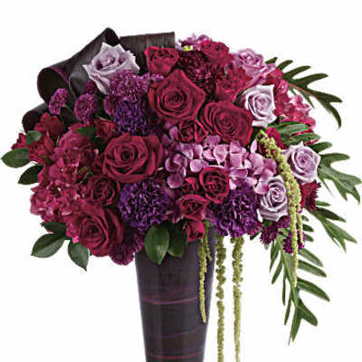Tall arrangement of red and purple roses with mixed blooms in a dark glass vase