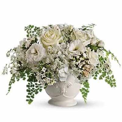 Low white urn of white roses and blooms with trailing ferns in a full rounded arrangement