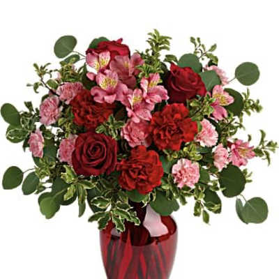 Red and pink roses and carnations with alstroemeria arranged in a red glass vase