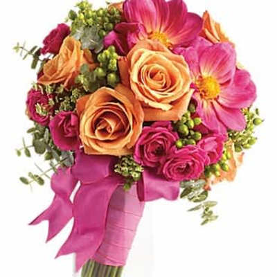 Bright bouquet of orange roses and hot pink blooms in a clear glass vase wrapped with a pink ribbon.