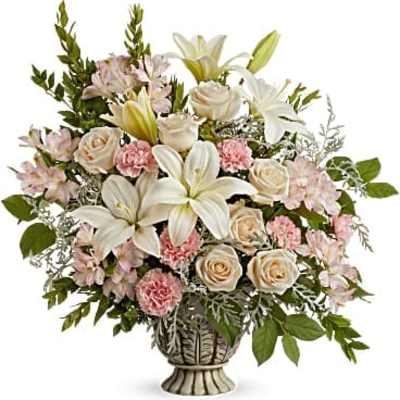 Tall arrangement of white lilies, cream roses, and pink carnations in an urn-style vase