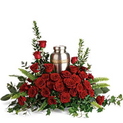 Silver cremation urn surrounded by a bed of red roses and trailing greenery.