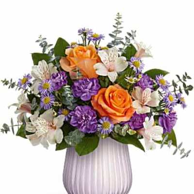 Arrangement of orange roses, purple carnations, asters, and white alstroemeria in a pale lavender ribbed vase