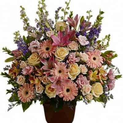Tall arrangement of pastel roses, gerbera daisies, lilies and purple flowers in a dark pedestal vase