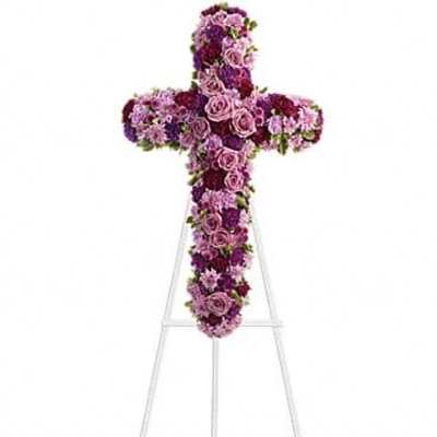 Tall floral cross in shades of pink and purple displayed on a white metal easel stand