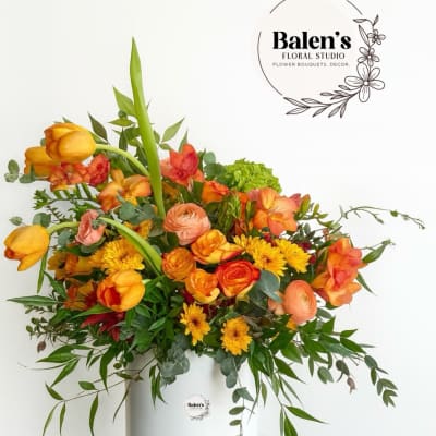 Orange and yellow mixed flower arrangement in a white hatbox