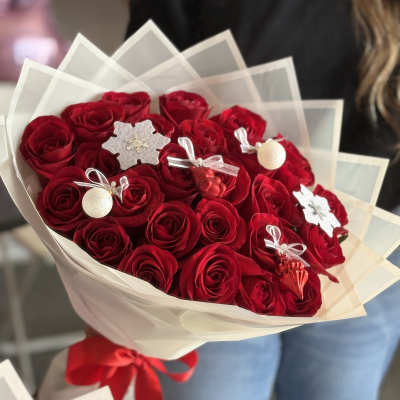 Bouquet of red roses wrapped in white paper with small holiday ornaments