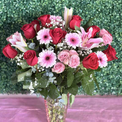 Bouquet of red and pink roses with lilies and pink daisies in a glass vase