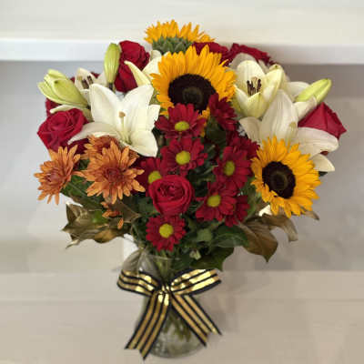 Mixed bouquet of sunflowers, lilies, roses, and daisies in a glass vase
