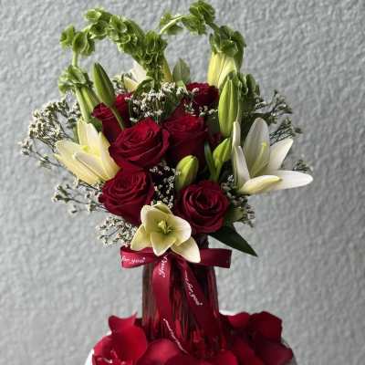 Red roses and white lilies in a red vase with rose petals