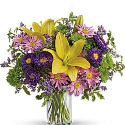 Mixed bouquet of yellow lilies, purple and pink daisies in a clear glass vase