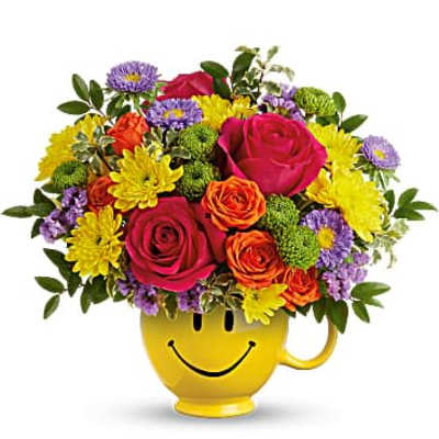 Bright mixed bouquet of roses and daisies in a yellow smiley-face mug