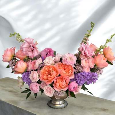 Pink and peach roses arranged with purple flowers in a silver vase.