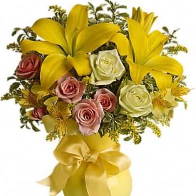 Yellow lilies and mixed pink and white roses in a round yellow vase with a large satin bow