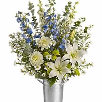 Tall arrangement of white lilies, mums, and blue delphinium in a silver metal bucket.