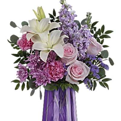 Mixed bouquet of white lilies, pink roses, and purple blooms in a faceted purple glass vase
