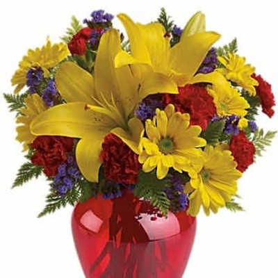 Bright bouquet of yellow lilies, yellow daisies and red carnations in a red glass vase