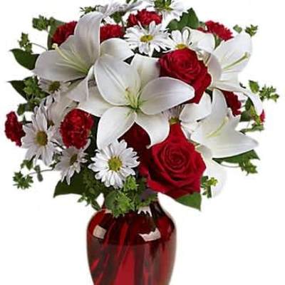 Red and white bouquet with lilies, roses, daisies, and carnations in a red glass vase