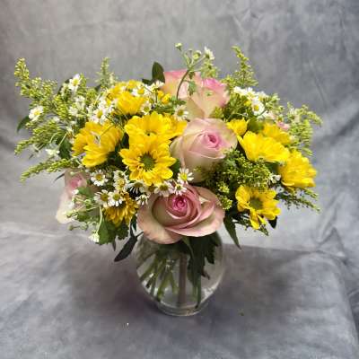 Pink roses and yellow daisies in a clear glass vase