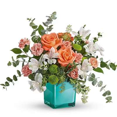 Peach roses and white flowers in a turquoise glass vase