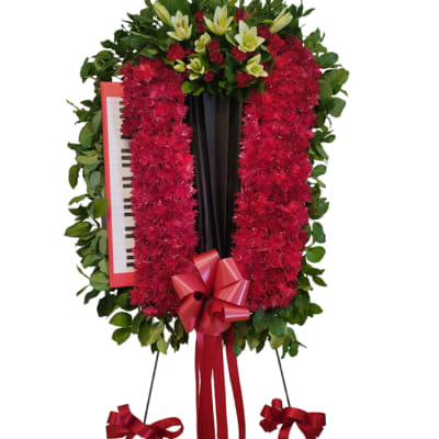Standing floral wreath with red flowers, lilies, and a piano inset