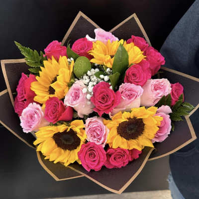 Bouquet of pink roses and yellow sunflowers wrapped in dark paper