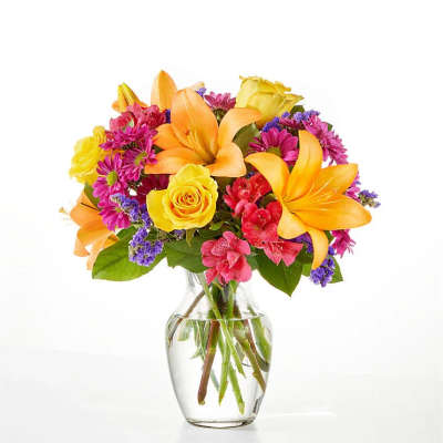 Bouquet of orange lilies, yellow roses, and pink flowers in a clear glass vase