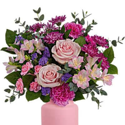 Pink and purple mixed flower arrangement with roses and carnations in a matte pink vase