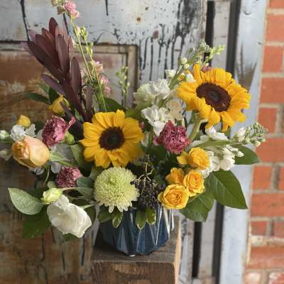 Mixed bouquet with sunflowers, roses, and white blooms in a blue vase