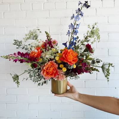Colorful mixed bouquet in a gold vase with orange, blue, and magenta flowers