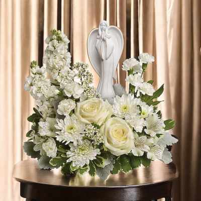 White floral arrangement with roses and daisies around a praying angel statue
