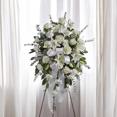 White floral standing spray with lilies, roses, and ribbon