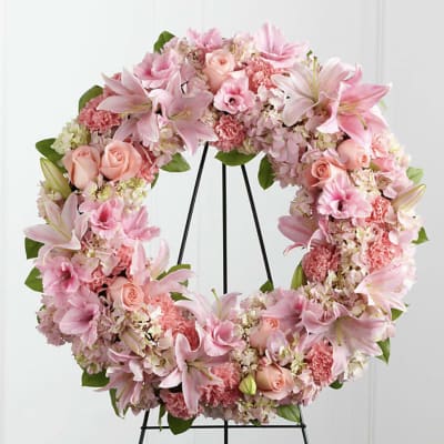 Pink floral wreath with lilies, roses, and carnations on a black stand