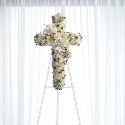 White floral cross arrangement on a stand with roses and lilies