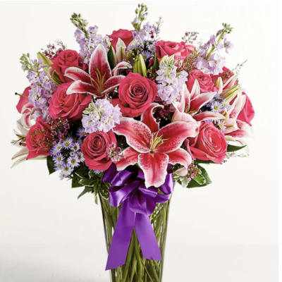 Pink roses and lilies in a clear glass vase with a purple ribbon