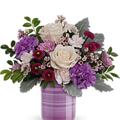Compact bouquet of ivory roses and purple blooms in a striped lavender ceramic vase
