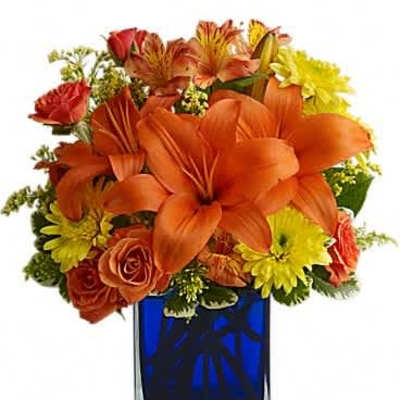 Bright arrangement of orange lilies, roses, and yellow blooms in a blue glass cube vase