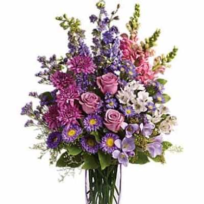 Tall arrangement of purple asters, pink roses, and mixed blooms in a clear glass vase