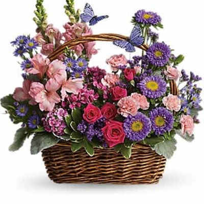 Wicker basket of purple asters, pink roses, carnations, and snapdragons with decorative blue butterflies.
