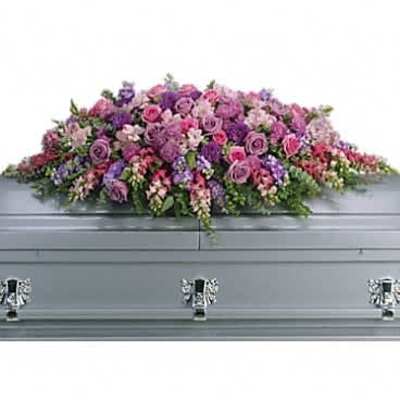 Pink and purple casket spray with roses and mixed flowers resting on a silver casket