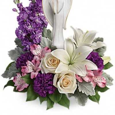Sympathy arrangement with white lilies, cream roses, purple flowers and an angel figurine.